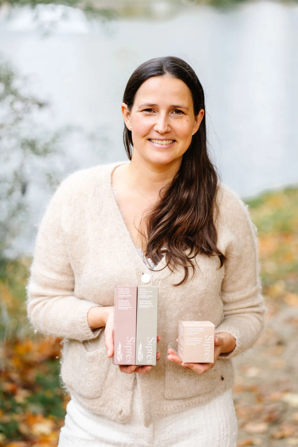Camille, fondatrice de Siprès, souriante en extérieur, tenant plusieurs boîtes de soins Siprès